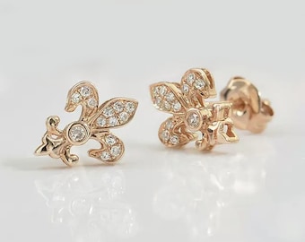 Könnte beinhalten: Ein Paar goldfarbene Ohrringe mit einem Fleur-de-lis-Design. Jeder Ohrring ist mit kleinen, klaren Steinen verziert.