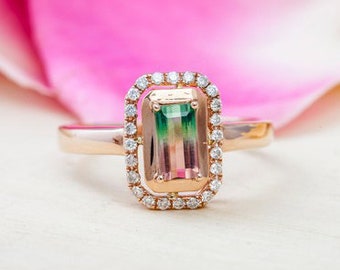 May include: A rose gold ring with a rectangular, multi-colored gemstone surrounded by a halo of small diamonds.