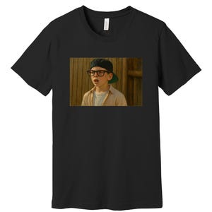 Puede incluir: Camiseta negra con una imagen rectangular de una persona joven con gafas, una gorra de béisbol y una camisa de color claro. La imagen está situada sobre un fondo de madera. La persona parece sorprendida o en estado de shock.