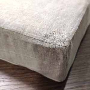 Puede incluir: Primer plano de un coj&iacute;n de lino beige con una costura bien cosida. El coj&iacute;n est&aacute; sobre una superficie de madera.
