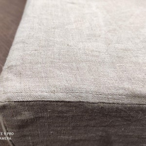 Puede incluir: Primer plano de una tela de lino beige con una textura sutil. La tela est&aacute; doblada, creando una costura.