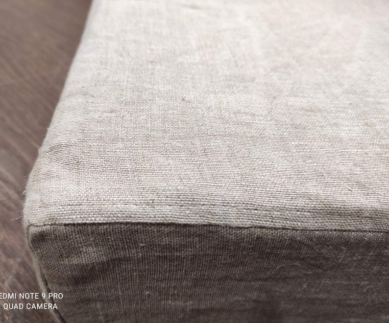 Puede incluir: Primer plano de una tela de lino beige con una textura sutil. La tela est&aacute; doblada, creando una costura.