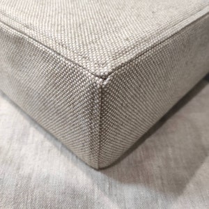 May include: Close-up of a beige fabric corner with a subtle woven pattern. The fabric is soft and textured, with a slightly raised seam along the edge.