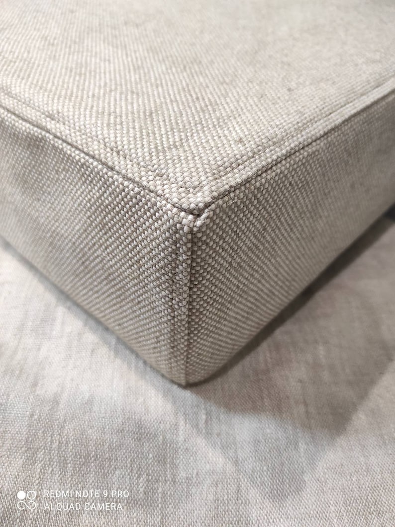May include: Close-up of a beige fabric corner with a subtle woven pattern. The fabric is soft and textured, with a slightly raised seam along the edge.
