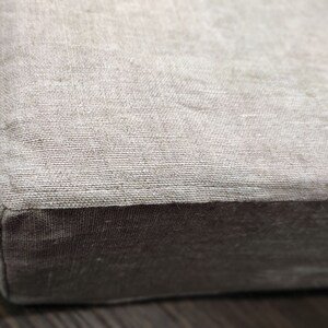 Puede incluir: Un primer plano de un coj&iacute;n de lino beige con un borde de tela marr&oacute;n. El coj&iacute;n es suave y texturizado.
