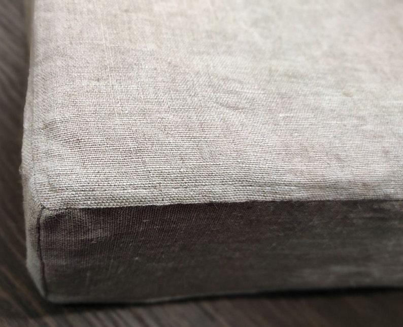 Puede incluir: Un primer plano de un coj&iacute;n de lino beige con un borde de tela marr&oacute;n. El coj&iacute;n es suave y texturizado.