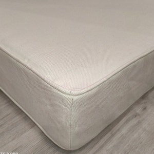 May include: Close-up of a white, rectangular cushion with a stitched seam around the edge. The cushion is made of a soft, textured fabric.