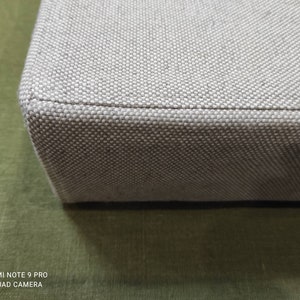May include: Close-up of the edge of a light gray fabric storage box. The fabric has a woven texture.