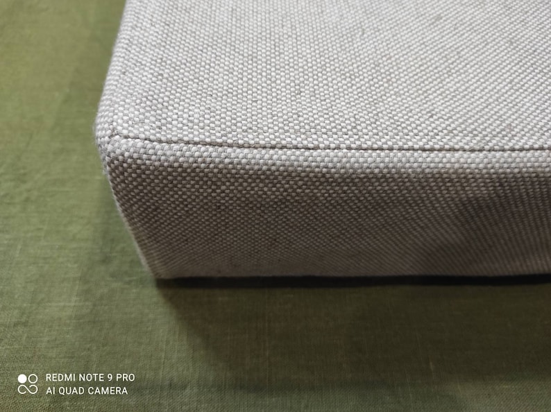 May include: Close-up of the edge of a light gray fabric storage box. The fabric has a woven texture.