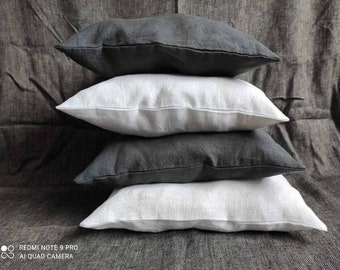 May include: A stack of four throw pillows, two white and two dark gray, arranged on a textured gray surface.