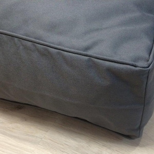 以下が含まれることがあります： 厚いパッド入りクッションと縁に縫い目がある灰色の長方形の犬用ベッドです。