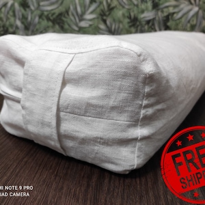 May include: White linen meditation cushion with a zipper closure. The cushion is rectangular and has a rounded top. The text "FREE SHIPPING" is stamped in red on a white circle.