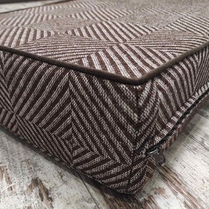 May include: A brown and white patterned cushion with a zipper closure. The cushion is made of a soft, textured fabric.
