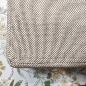 May include: Close-up of a beige fabric with a woven texture. The fabric has a subtle sheen and a slightly rough feel.
