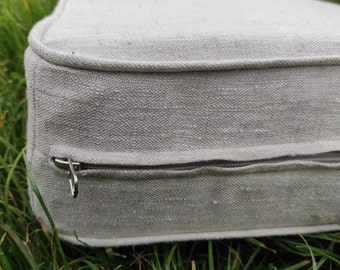 May include: A close-up of a light gray cushion with a zipper closure. The cushion is made of a textured fabric and has a subtle sheen.