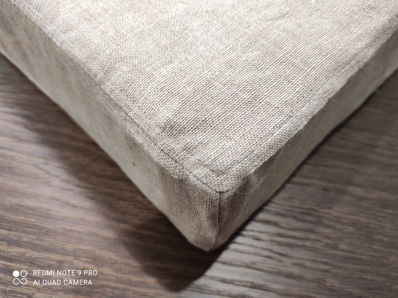Puede incluir: Primer plano de una esquina de tela de lino beige, mostrando el detalle de las costuras. La tela es texturizada y tiene un brillo sutil.