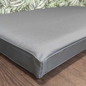 May include: A grey rectangular cushion with a thick, stitched border. The cushion is made of a soft, textured fabric.