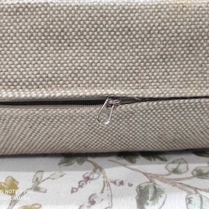May include: A close-up of a beige cushion with a zipper closure. The zipper is made of metal and has a silver finish.
