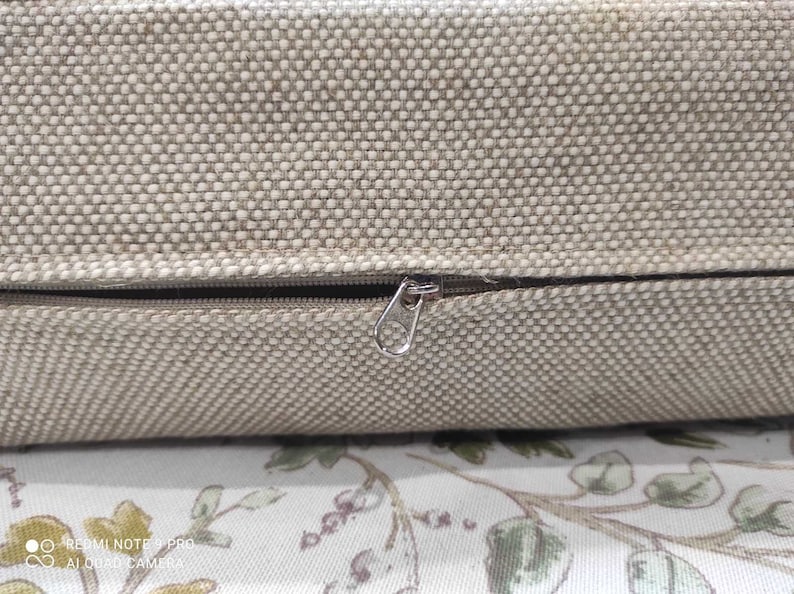 May include: A close-up of a beige cushion with a zipper closure. The zipper is made of metal and has a silver finish.