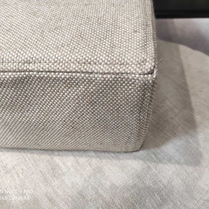 May include: Close-up of the beige fabric edge of a piece of furniture. The fabric has a woven texture.