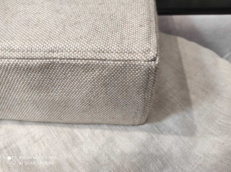 May include: Close-up of the beige fabric edge of a piece of furniture. The fabric has a woven texture.