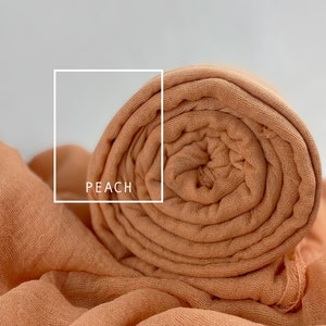 May include: A peach-colored fabric scarf rolled up. The fabric is soft and has a slightly textured surface. The text "PEACH" is written in white on a white rectangle.