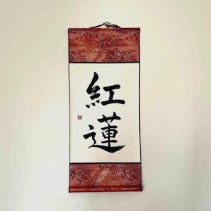 May include: A rectangular wall scroll with Japanese calligraphy. The scroll features a white background with black characters and a red patterned border. The top and bottom borders have a textured, swirling design.