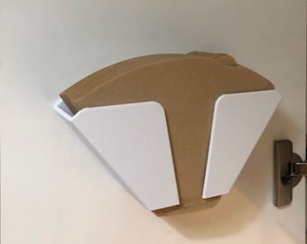 May include: A white, V-shaped wall-mounted holder containing a stack of brown, cone-shaped paper coffee filters. The holder is attached to a flat, white surface, providing a storage solution for keeping coffee filters organized and accessible.