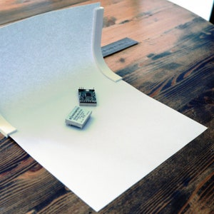 May include: Two small electronic circuit boards on a white backdrop. The boards are white with black markings and are sitting on a white surface.