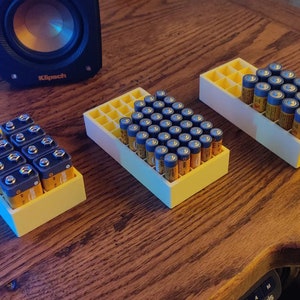 May include: Three yellow plastic battery organizers with different sizes. The largest organizer is filled with AA batteries, the medium organizer is filled with AAA batteries, and the smallest organizer is empty.