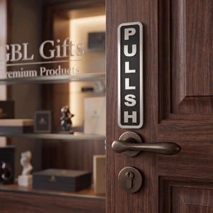 May include: A dark brown wooden door with a silver and black "PULLSH" sign. The door has a bronze handle and a keyhole. In the background, a glass display case with the text "GBL Gifts Premium Products" is visible.