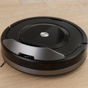 May include: A black and silver robotic vacuum cleaner on a light wood floor. The vacuum has a circular design with a silver accent and a central metallic button. The text "GBL Gifts" is visible in the background.