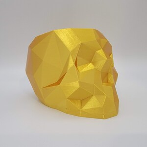 May include: A gold-colored, geometric skull planter. The skull is made of a smooth, shiny material and has a hollow interior.