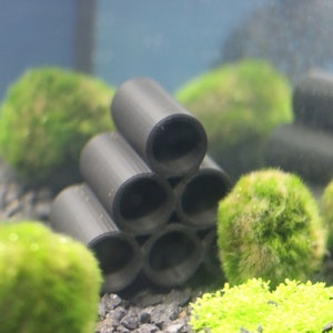 Pode incluir: Caverna de aqu&aacute;rio de cer&acirc;mica preta com seis aberturas, empilhadas em forma de pir&acirc;mide. A caverna &eacute; cercada por bolas de musgo verde e cascalho.