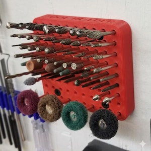 May include: A red tool holder with various drill bits and polishing wheels. The holder is mounted on a wall and has the words "TOOL HOLDER" printed on it. The drill bits are of different shapes and sizes.