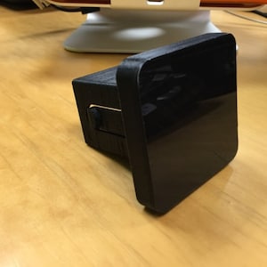 May include: A black, rectangular device with a glossy, reflective surface. The device is mounted on a black, textured base. The item is positioned on a light-colored wooden surface.