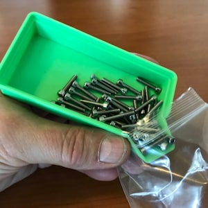 May include: A green plastic tray filled with silver screws, being poured into a clear plastic bag.