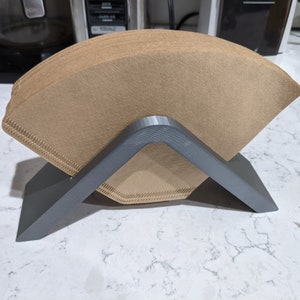 May include: A gray plastic coffee filter holder with a stack of brown paper coffee filters.