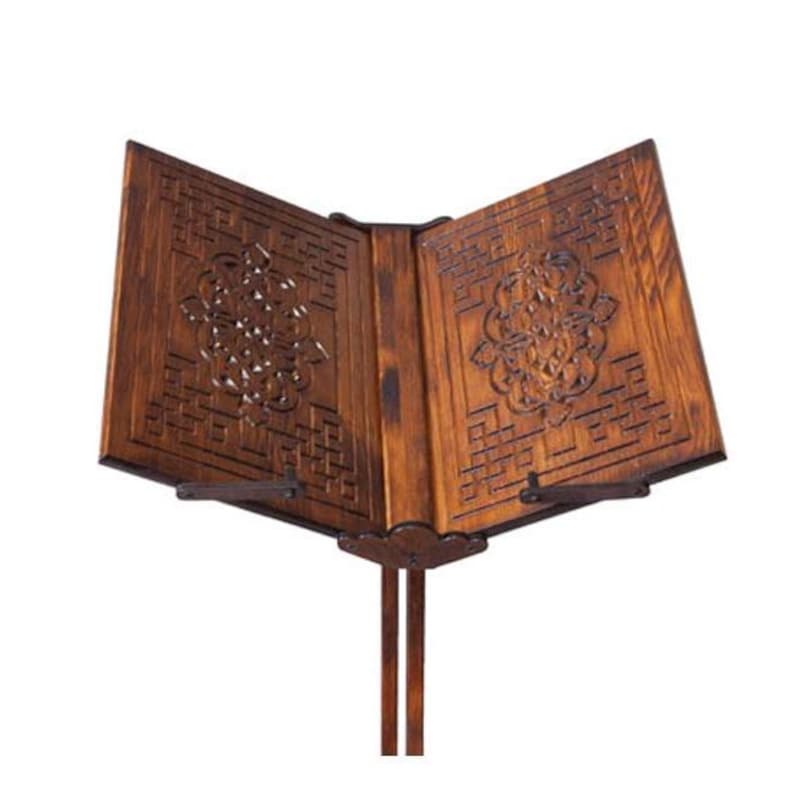 May include: A dark brown wooden book stand with detailed carved patterns. The stand has an open design, ready to hold a book, and is supported by a vertical stand. The carved design includes a floral motif.