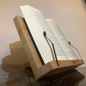 May include: A wooden book stand with metal page holders. The stand is made of natural wood and has a simple, elegant design. It is perfect for holding books, cookbooks, or other documents.