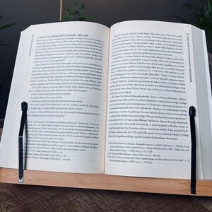May include: A close-up of an open book with a black page holder. The book is open to a page with text in Turkish. The text discusses the history of the Faculty of Law at Istanbul University.