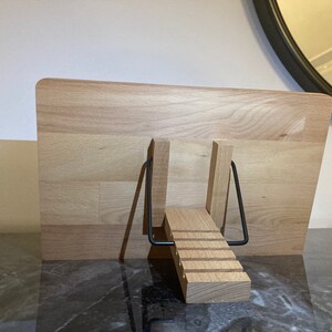 May include: A wooden book stand with a black metal frame. The stand is made of light wood and has a stepped design.