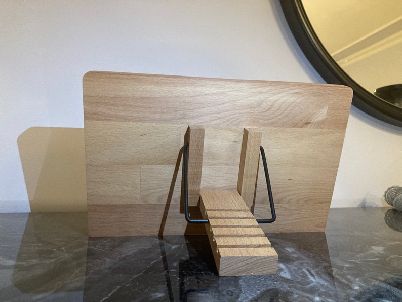 May include: A wooden book stand with a black metal frame. The stand is made of light wood and has a stepped design.
