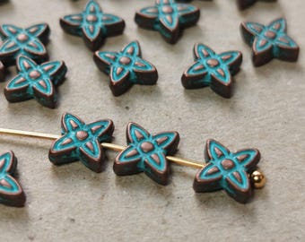 May include: A collection of teal blue and copper star-shaped beads with intricate designs. The beads are scattered on a light gray surface.
