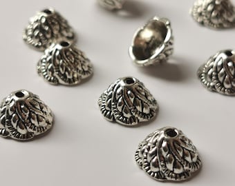 Op de afbeelding: Zilveren metalen kegelvormige kralen met een decoratief ontwerp. De kralen hebben een gat aan de bovenkant om te rijgen.