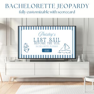 Op de afbeelding: Een witte tv-meubel met een groot flatscreen-tv waarop een "Bachelorette Jeopardy"-spel wordt weergegeven. Het spel heeft een blauw-wit nautisch thema met de tekst "Paisley's Last Sail Before the Veil". De kamer heeft een wit tapijt en witte muren.