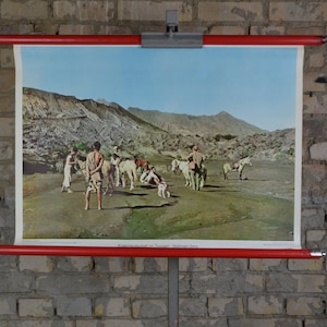 Puede incluir: Un cartel educativo vintage que representa a un grupo de personas a caballo en un paisaje desértico. El cartel está montado en un rodillo rojo y tiene el texto "Kameltreiber in der Toskana, Oberitalien" en la parte inferior.