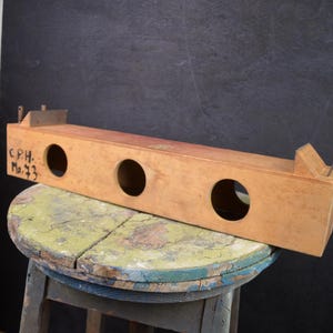 Può includere: Oggetto rettangolare in legno chiaro con tre fori circolari e la scritta "C.P.H. No. 73". Poggia su uno sgabello usurato e multicolore. Parti metalliche sono attaccate sopra. Probabilmente è uno strumento vintage.