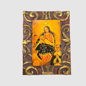 May include: A framed religious artwork with a gold and red ornate frame. The artwork depicts a woman holding a baby in her arms. The woman is wearing a blue and gold robe and a crown. The baby is wearing a white robe. The artwork is set against a yellow background.