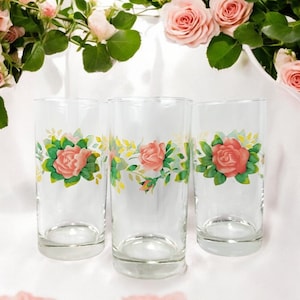 Könnte beinhalten: Drei klare Glas-Trinkgläser mit einem Design aus rosa Rosen und grünen Blättern.